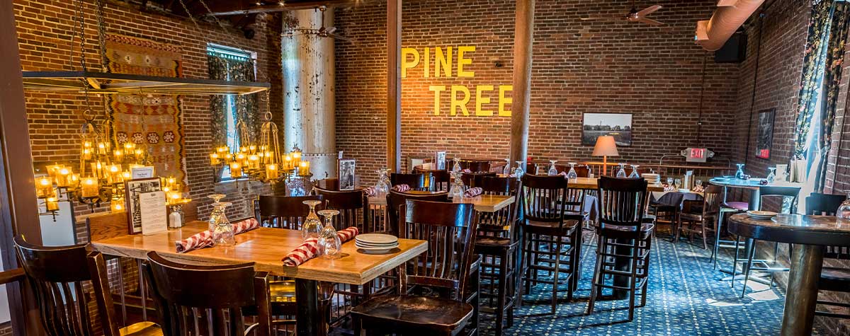 dining room with high top tables upstairs of fosters boiler room brick walls and "pine tree" lettered sign on back waller