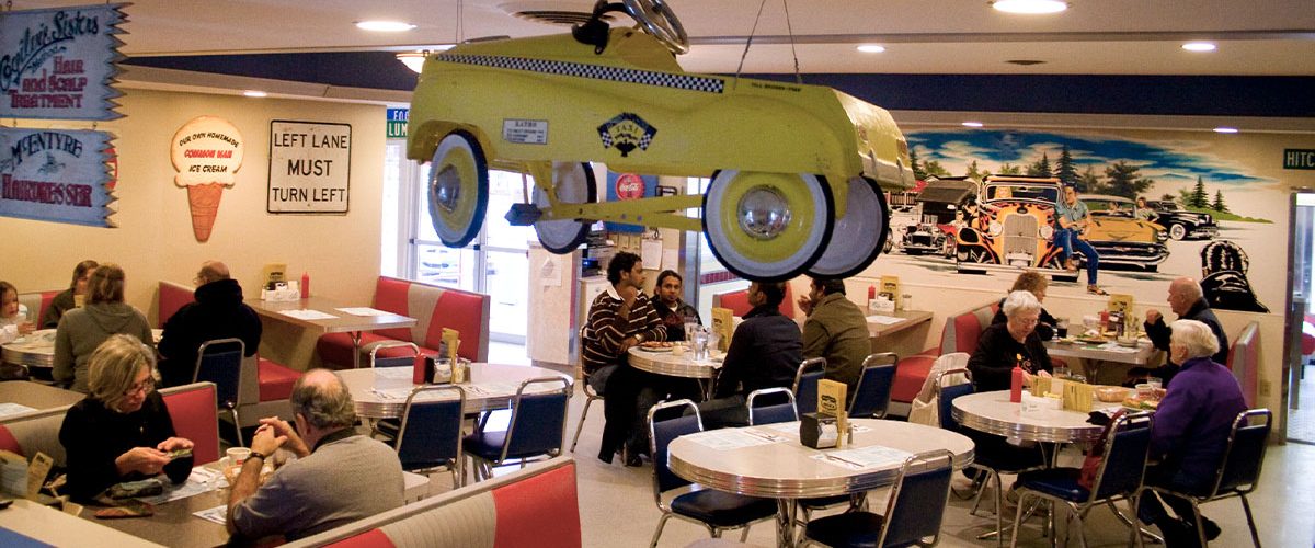 wider image of dining room, people dining, classic car decor hangs from ceiling