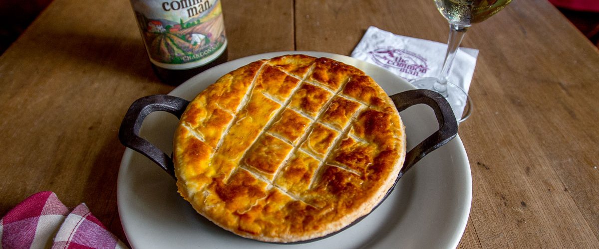 chicken pot pie in skillet on plate with common man wine bottle and full glass