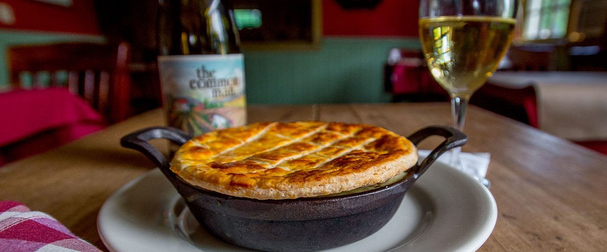 chicken pot pie in skillet on plate with common man wine and full wine glass in background