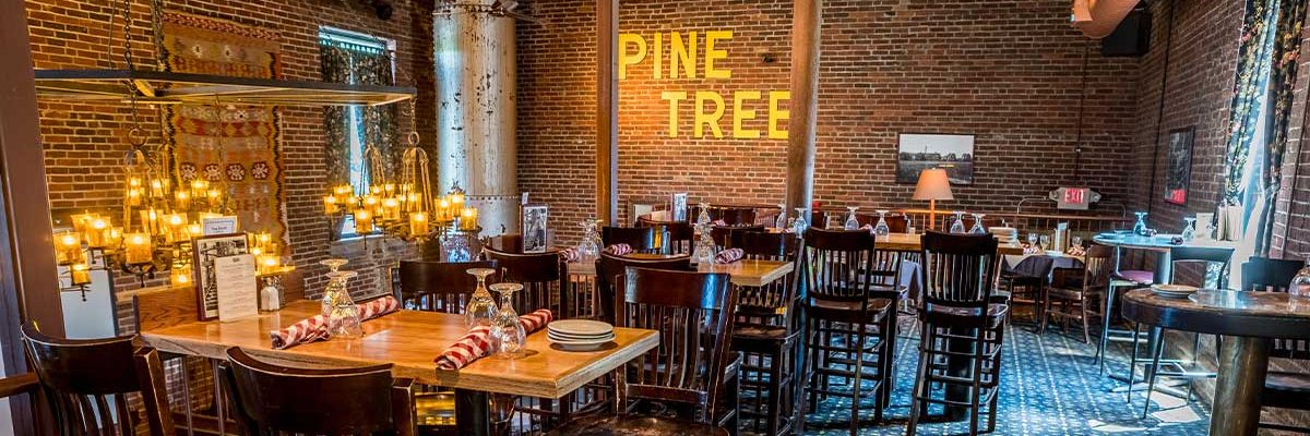 dining room with high top tables upstairs of fosters boiler room brick walls and "pine tree" lettered sign on back waller